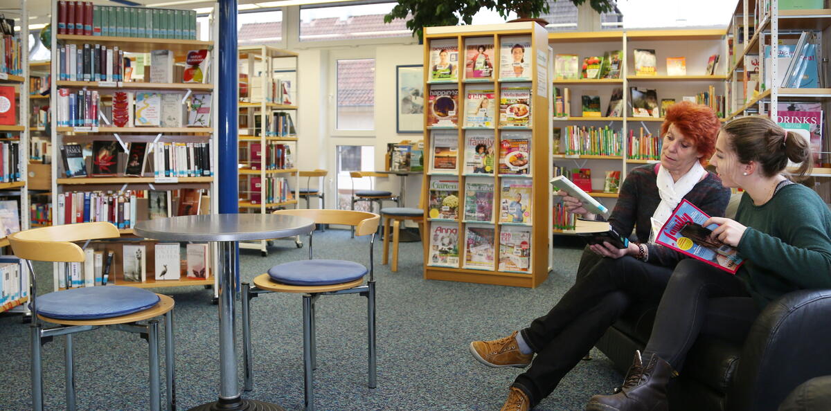 Bild vergrößern: Bücherregale der Gemeindebücherei Jockgrim. Zwei Frauen lesen in einem Buch.