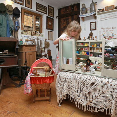 Bild vergrößern: Mädchen spielt mit antikem Kaufladen in der Ausstellung Leben und Arbeiten früher
